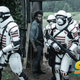 The well-armed and white-armored soldiers of the Commonwealth marches through a wooden gate.